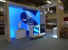 Custom Island Exhibit with Laminated Backlit Slatwall, Canopy, Pendant Lights, Backlit Logo, Double-sided Backlit Fabric Graphic, (3) Large Monitor Mounts, and (3) Custom Reception Counters